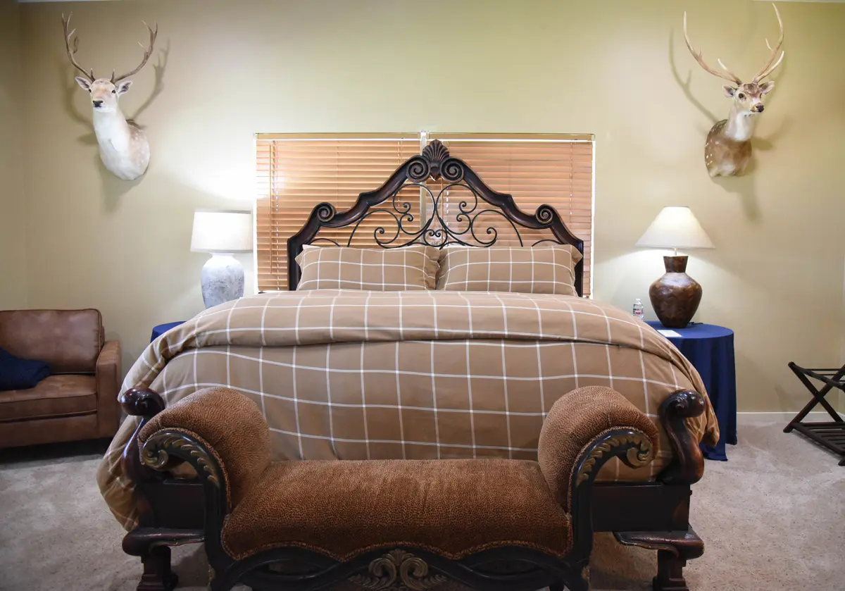 Large bed with brown checkered comforter and fancy, rustic headboard